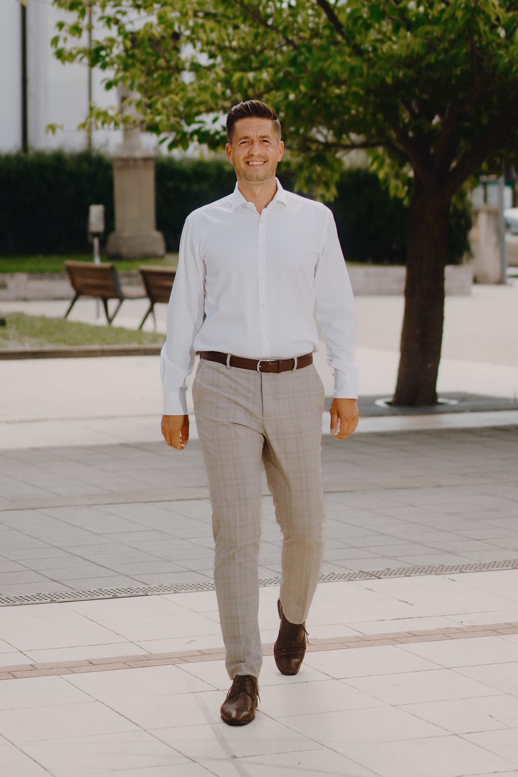 Roman Krištofík kráča po senickom námestí, v pozadí mariánsky stĺp a stromy